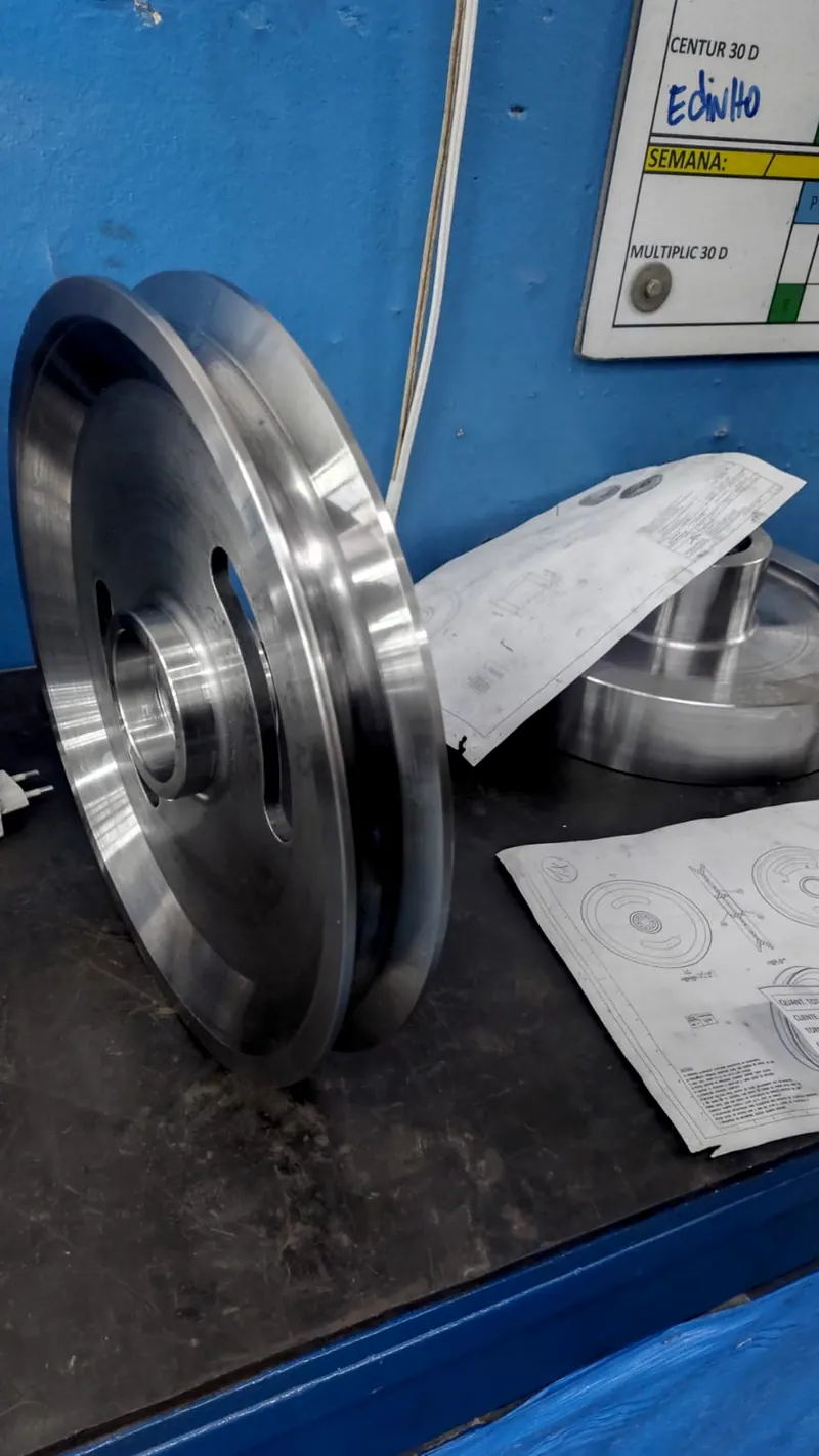 Peça redonda usinada em pé na bancada, ao lado do desenho técnico dela