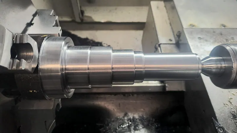 Eixo de aço preso na placa de um torno CNC, com o acabamento usinado brilhando